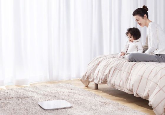 Mujer con su bebé sentada en la cama, mientras mira la  Mi Smart Scale 2